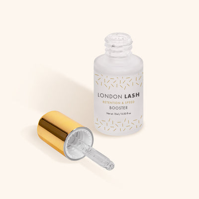 an open bottle of london lash booster in a frosted glass bottle with a gold lid. the lid is laying next to the bottle showing the pipette