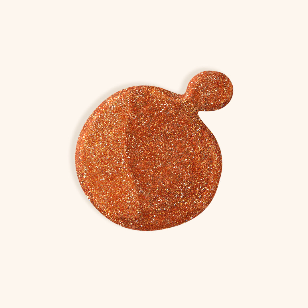 Glittery bronze nail polish in front of beige background