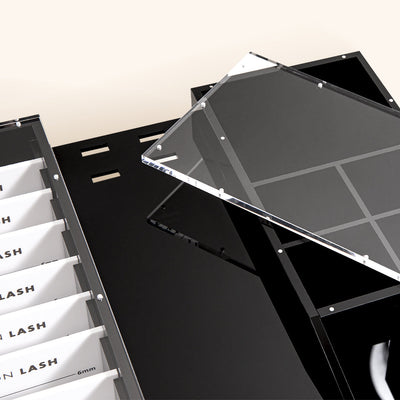 an acrylic organizer for eyelash extension supplies. ten slim lash palettes are shown as are slots for 4 pairs of tweezers and an extra section for cleansing brushes