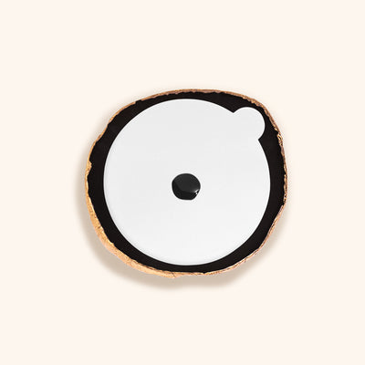a black agate stone for lash extensions glue. It has a painted gold edge. On the surface of the glue stone is a white sticker with a drop of lash glue in the centre