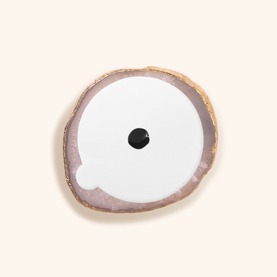 a white agate stone for lash extensions glue. It has a painted gold edge. On the surface of the glue stone is a white sticker with a drop of lash glue in the centre