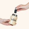 one hand holds the container while another hand holds a bottle of lash glue over the opening