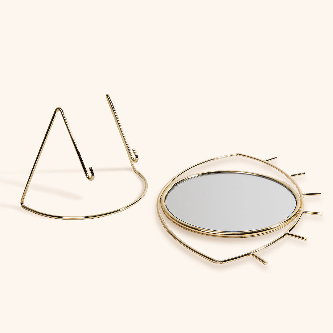 a gold eye shaped mirror lying next to its stand