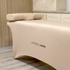 a beauty bed in a salon with a beige bed cover and matching memory foam neck pillow