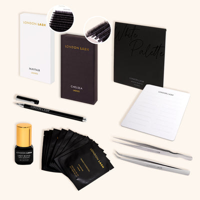 a flat lay of a lash extensions kit featuring lash glue, eyepatches, two trays of eyelash extensions a lash palette and two pairs of tweezers