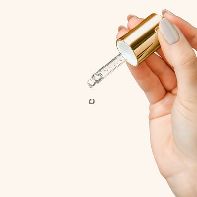 a hand holding the lid from a lash primer dispensing a drop of liquid from the pipette