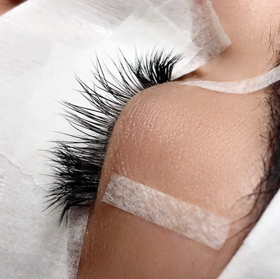two pieces of surgical tape being used to gently lift each end of the eyelid to make lash extension application easier.